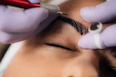 A beautician performing microblading on a client's eyebrows.