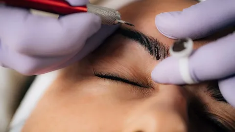 A beautician performing microblading on a client's eyebrows.